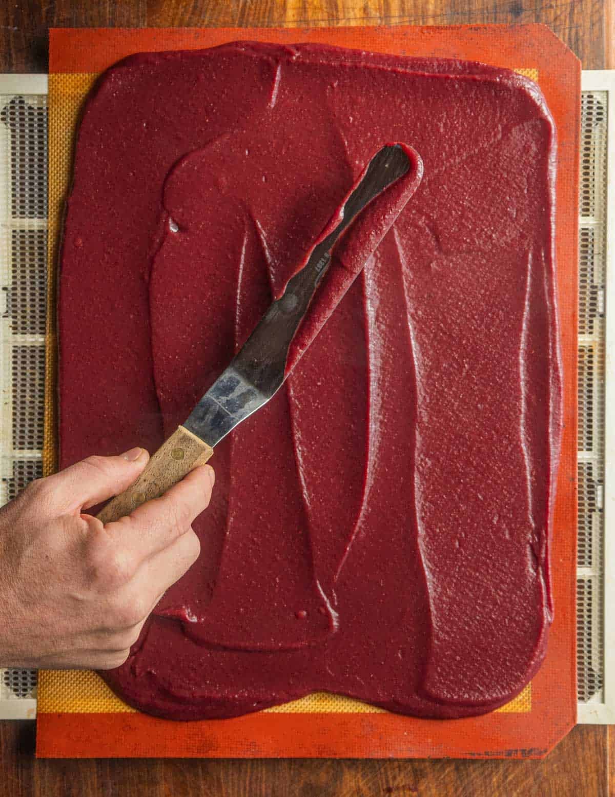 Spreading mixed apple and cranberry puree on a baking sheet lined with a silicone mat before dehydrating into fruit leather.