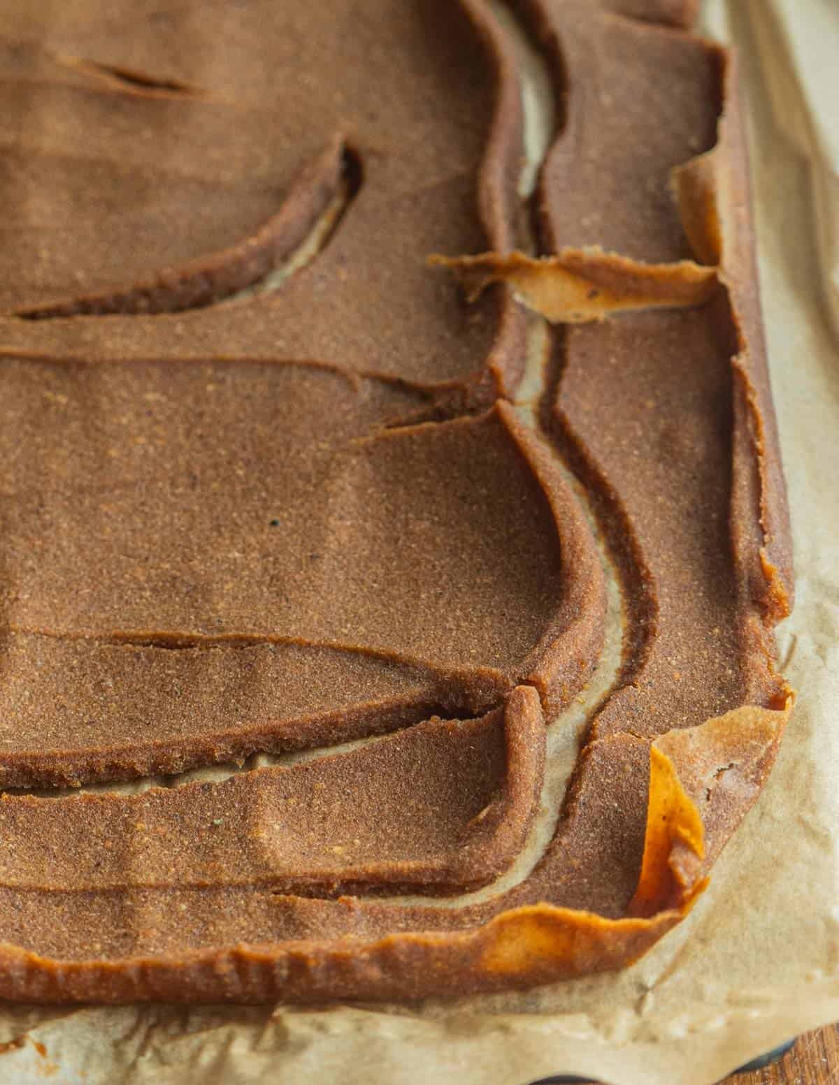 A close up image of persimmon leather on a sheet of parchment showing cracks in the fruit leather from drying.
