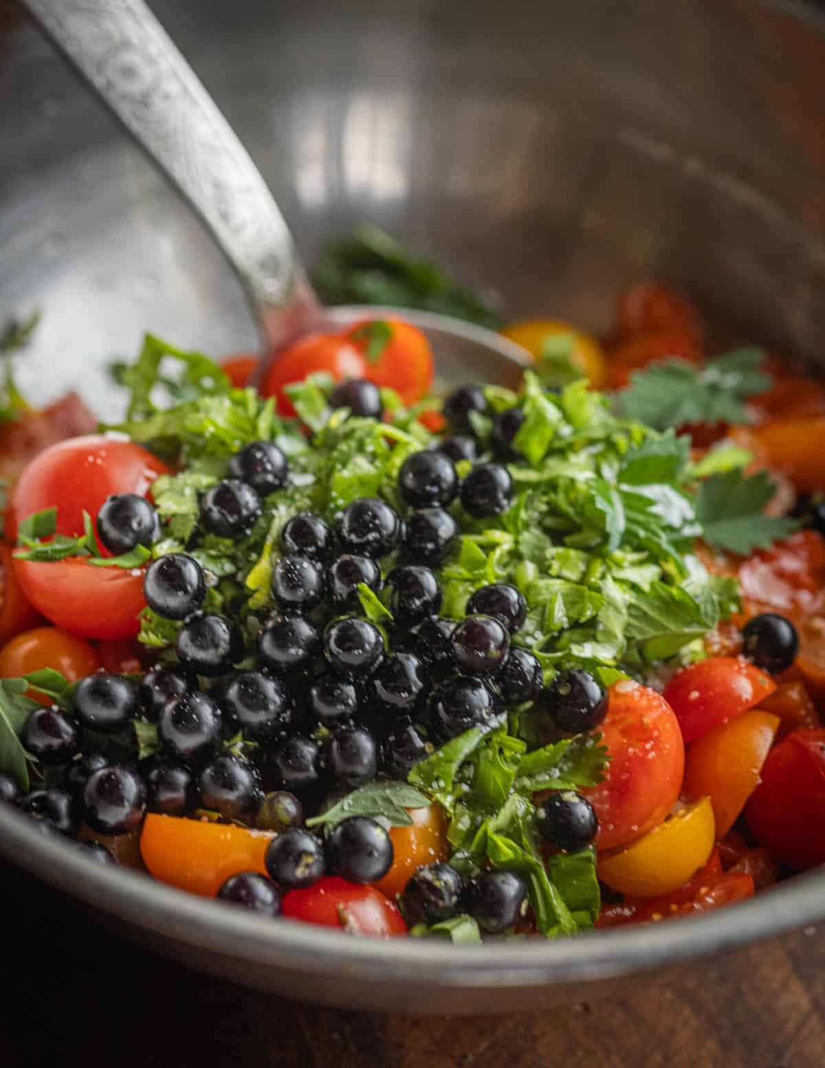 A close up image of black nightshade berries, tomatoes and peppers with herbs being mixed for a salad.