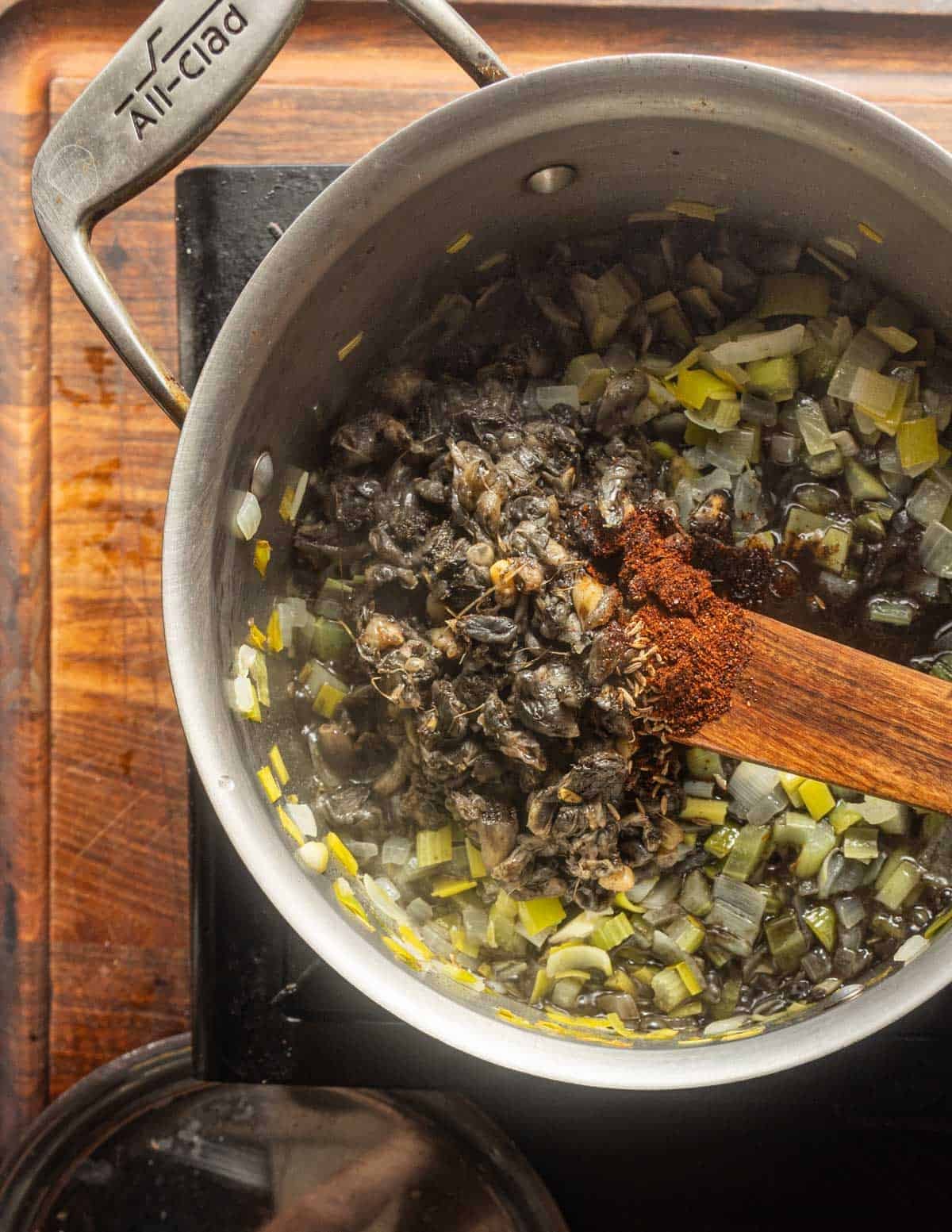 Adding frozen huitlacoche to a pot of cooked vegetables with cumin and chili powder.