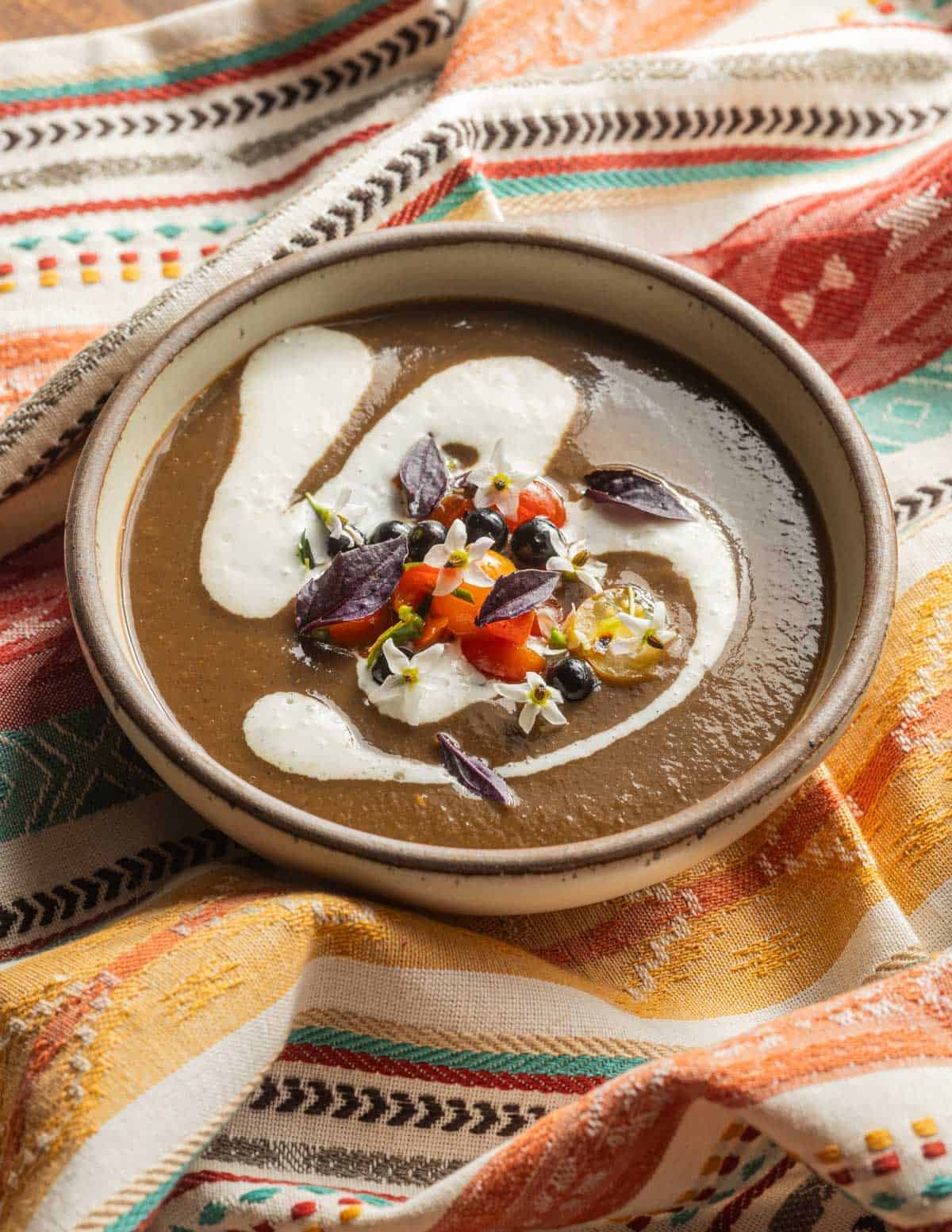 A bowl of sopa de huitlacoche on a Mexican napkin garnished with sour cream and tomato-herb salad.