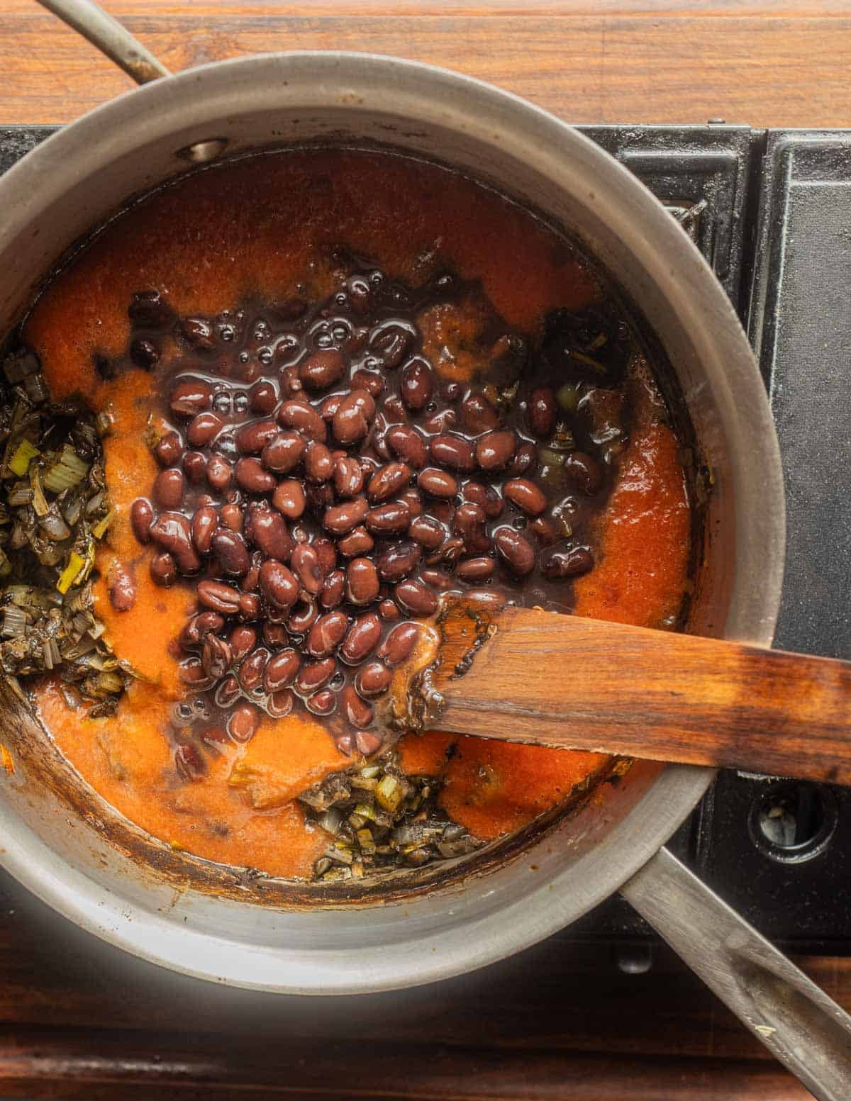Adding black beans and tomato puree to a pot of sopa de huitlacoche.