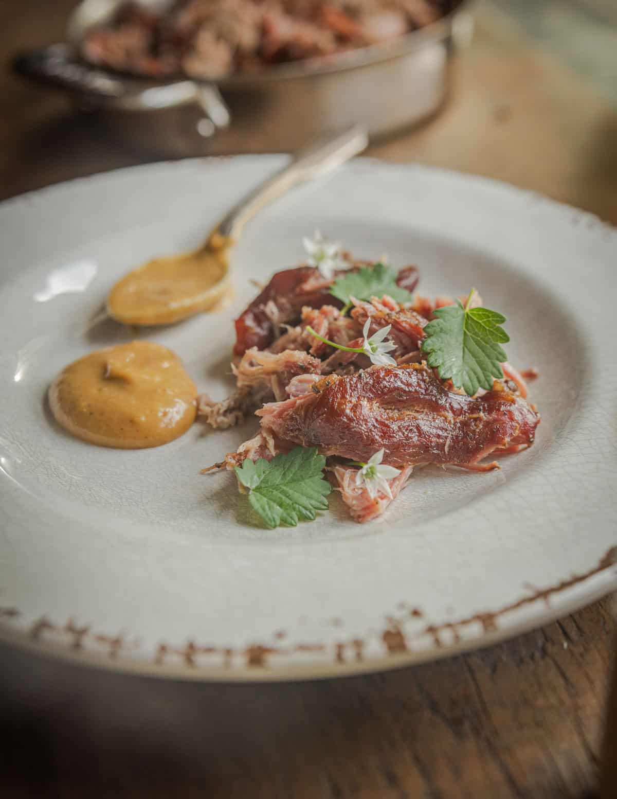 Smoked pork on a plate with a spoonful of paw paw sauce garnished with burnet leaves.