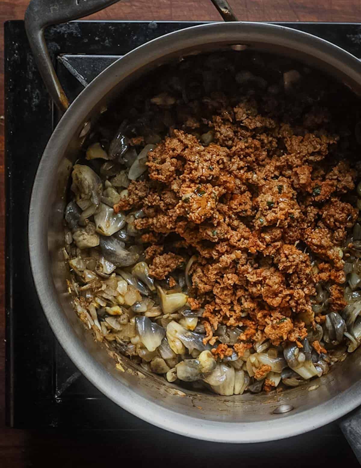 A soup pot showing chorizo sausage being added to a pot with huitlacoche mushrooms for soup.