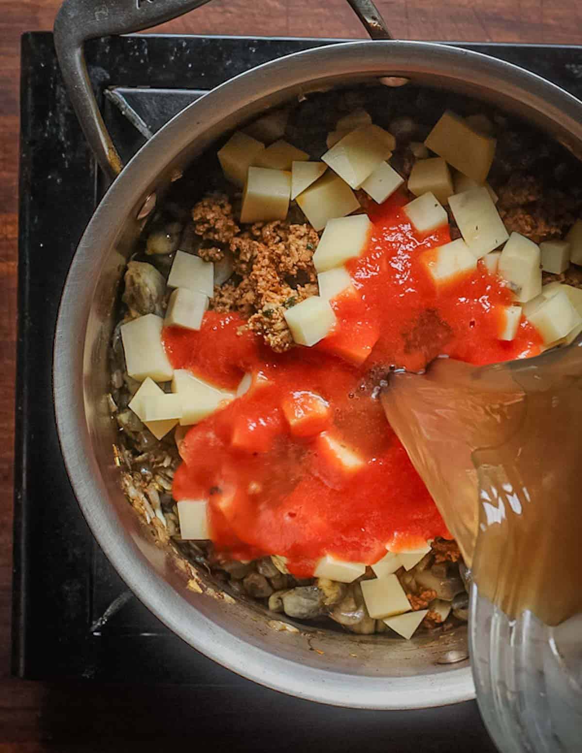Adding stock, tomato puree and diced potatoes to a pot of sopa de huitlacoche.